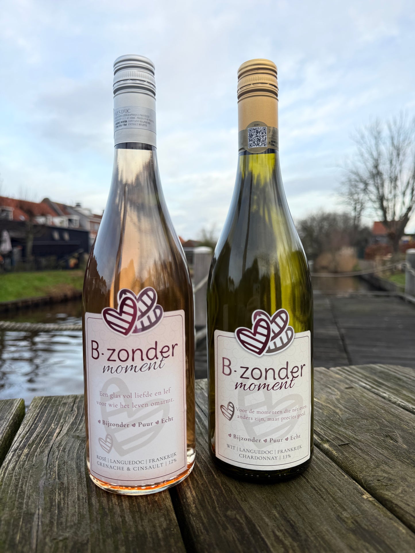 Twee flessen B-zonder moment wijn, rosé en chardonnay, op houten tafel bij water in Languedoc, Frankrijk