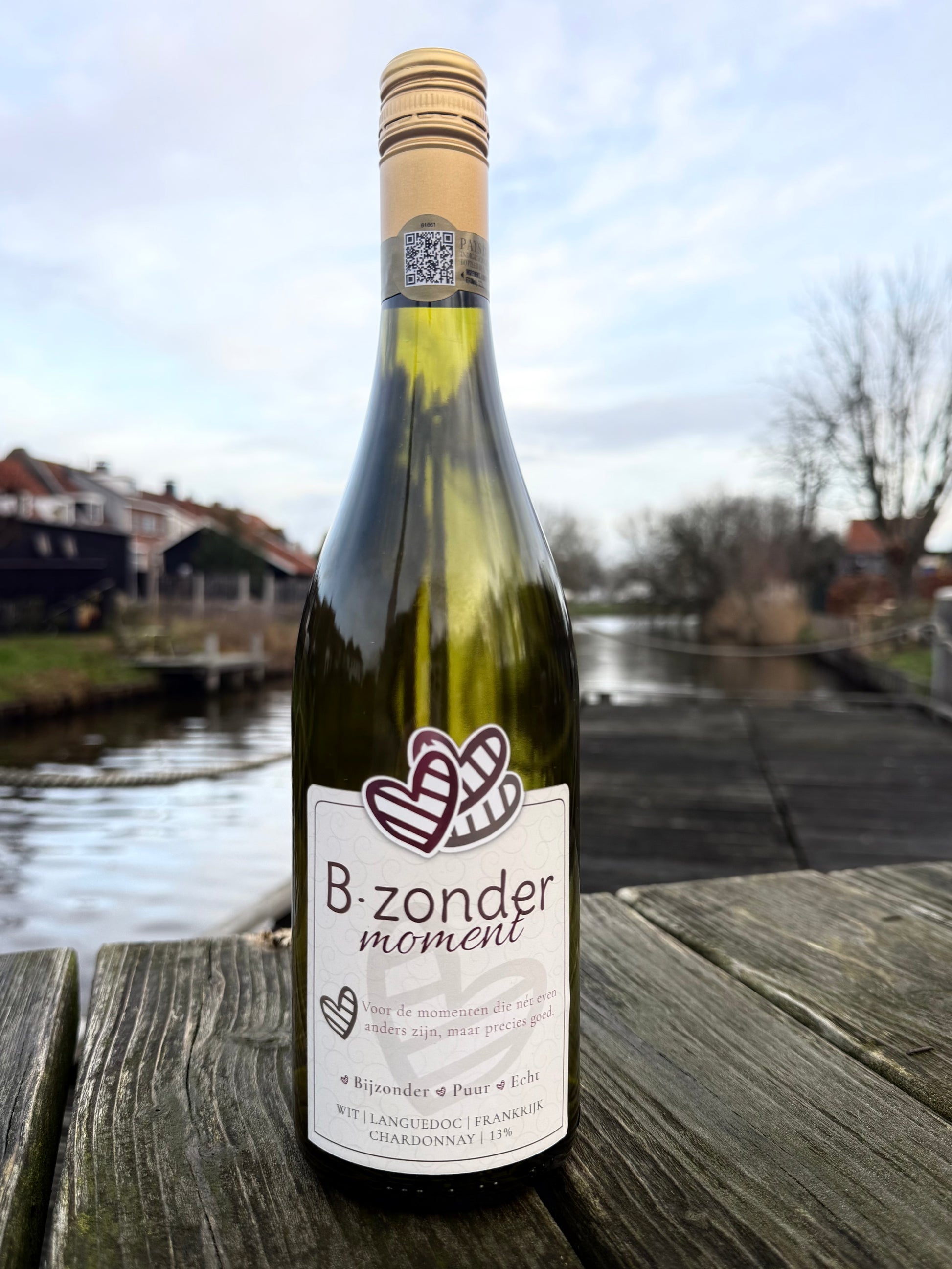 Fles B.zonder moment Chardonnay witte wijn op houten tafel bij water en huizen