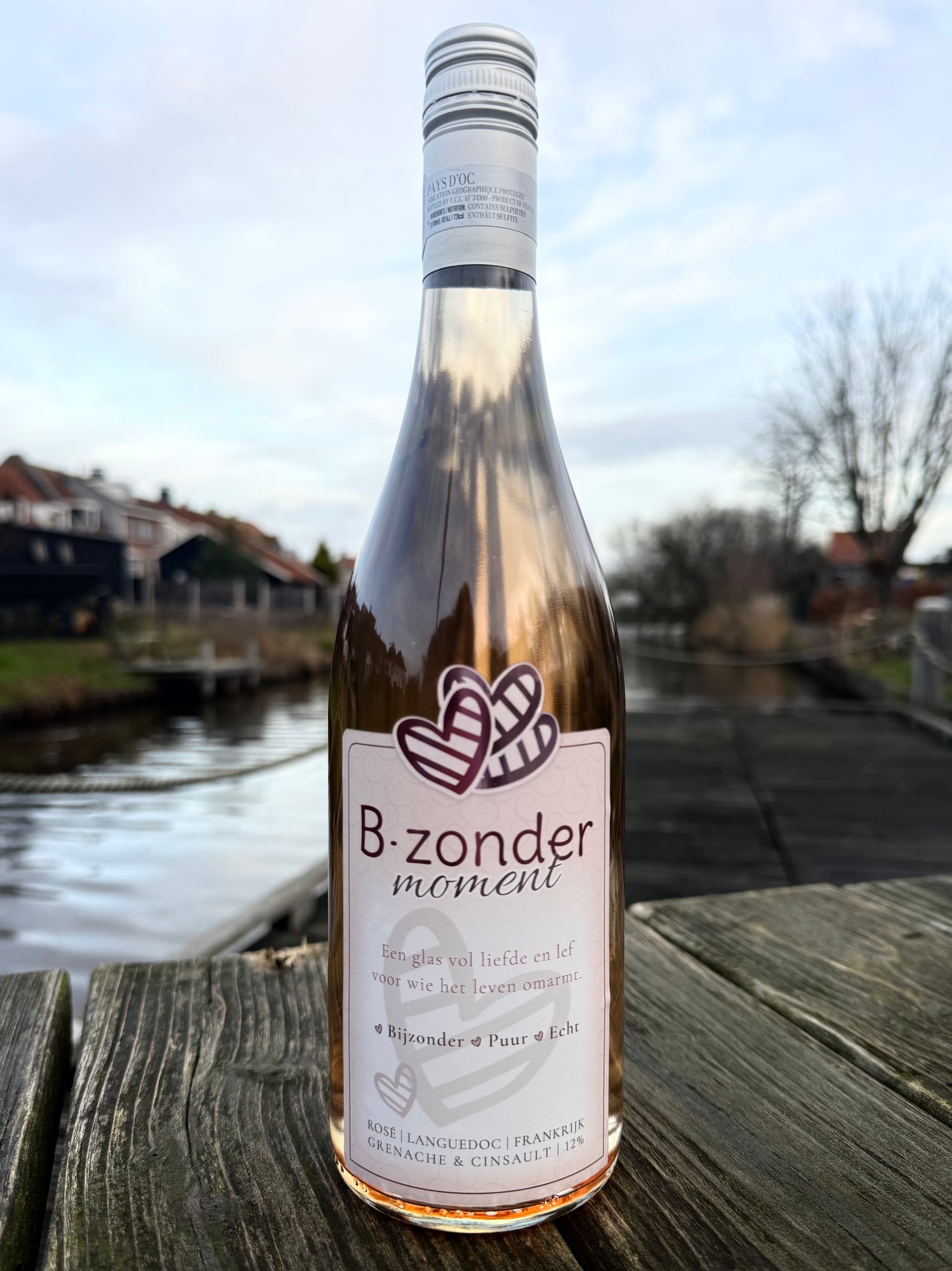 Fles B-zonder moment rosé wijn op houten tafel bij kanaal met huizen in achtergrond